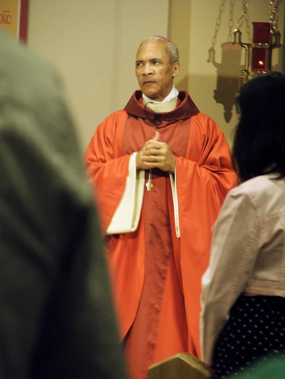 a priest wearing red is speaking to an older woman