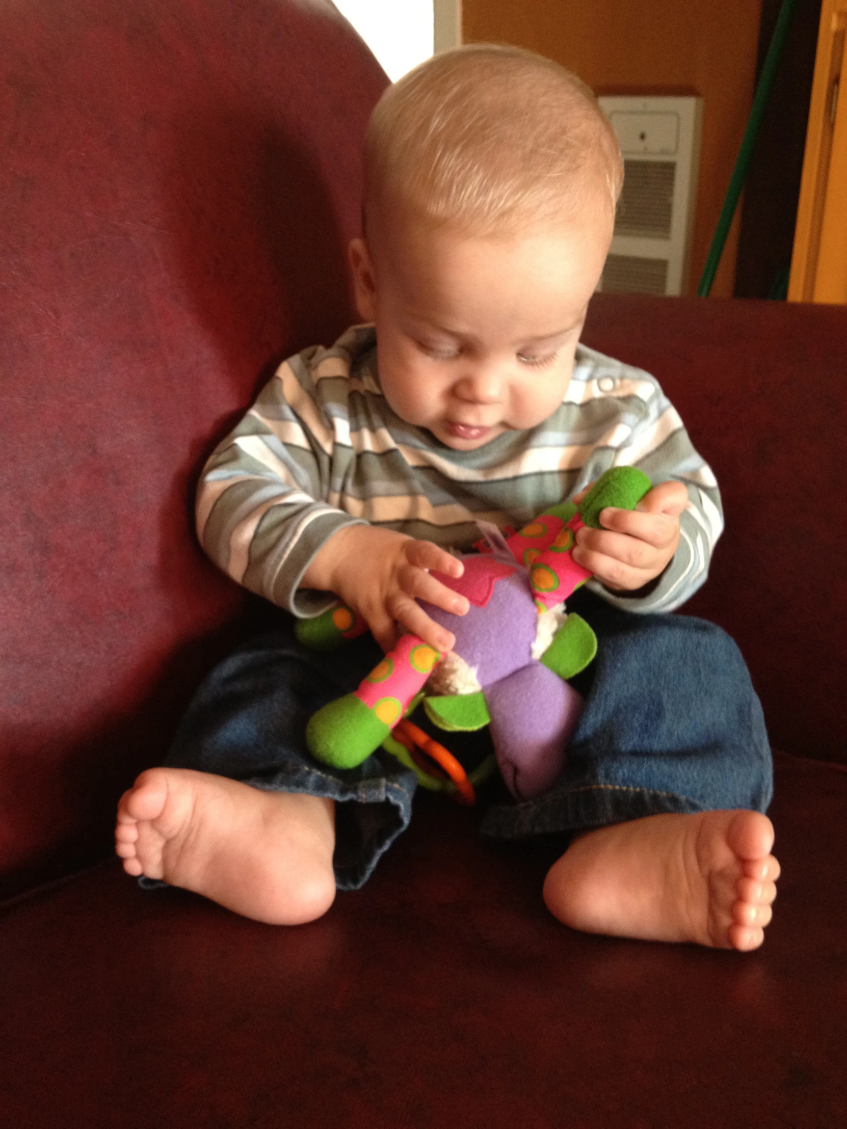 a toddler sits in a red chair holding a colorful teddy bear