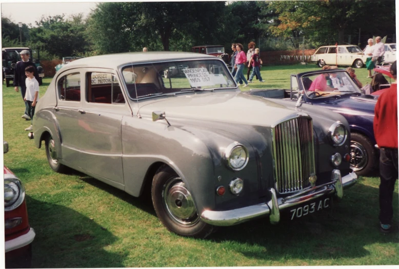 people are looking at an antique car on the grass