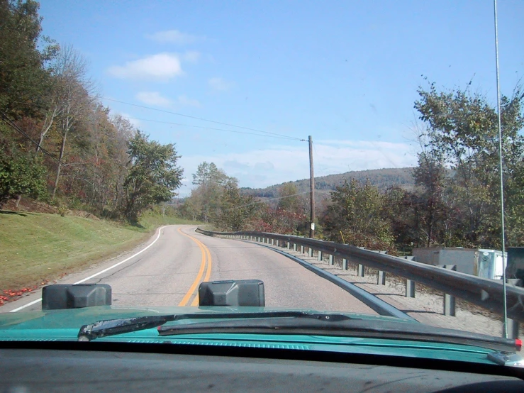 a view of an empty road and trees through the windshield of a car