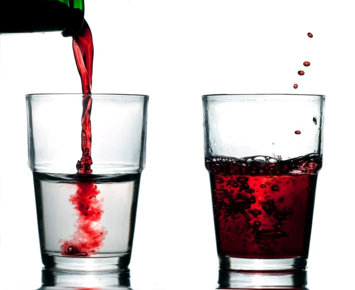 red liquid pouring out of a bottle into two glasses filled with different liquids