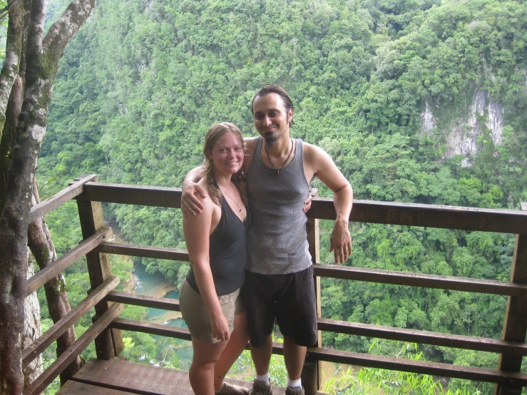 a woman standing next to a man on a bridge near trees