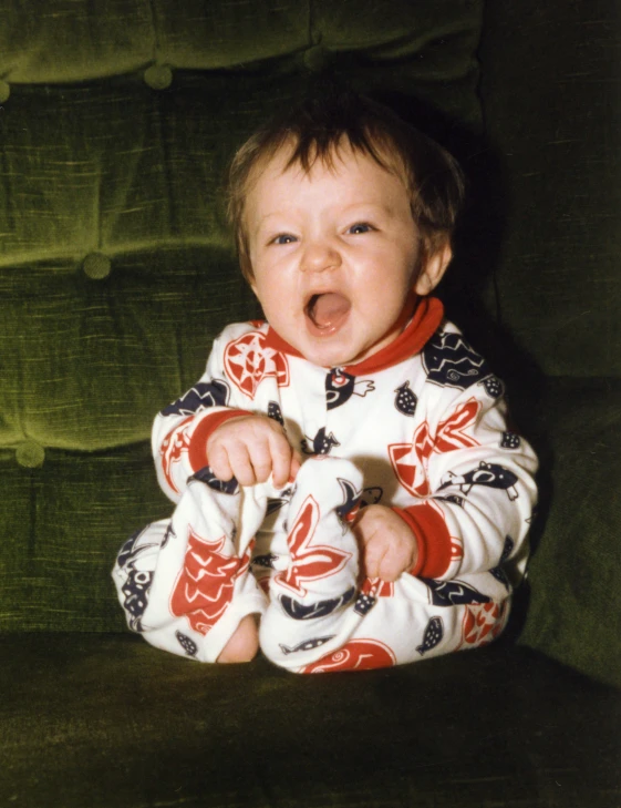 a small baby in pajamas sitting on a couch