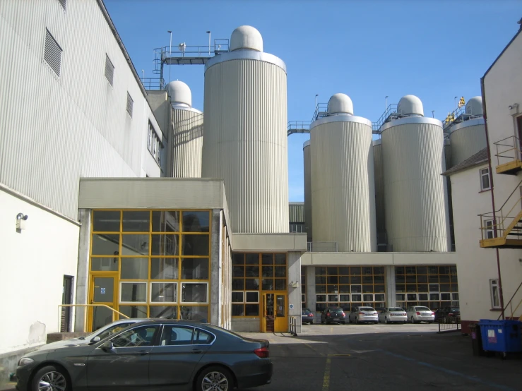 a grey car sitting in a parking lot next to cement silos