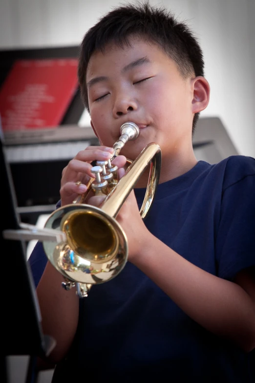 an asian  plays the trumpet in front of a laptop computer