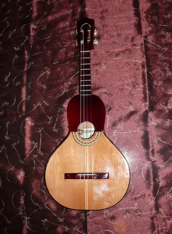 an old, used guitar is lying on a purple patterned cloth