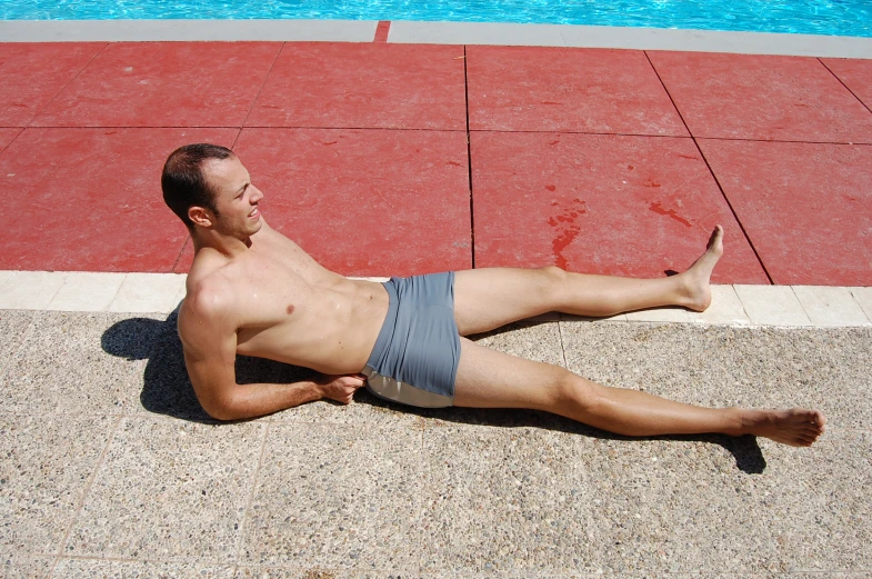 man wearing blue swim trunks laying next to pool in daylight