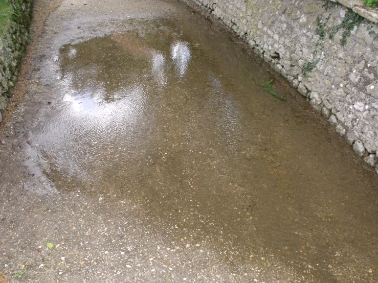 the sidewalk is covered with water next to the stone wall