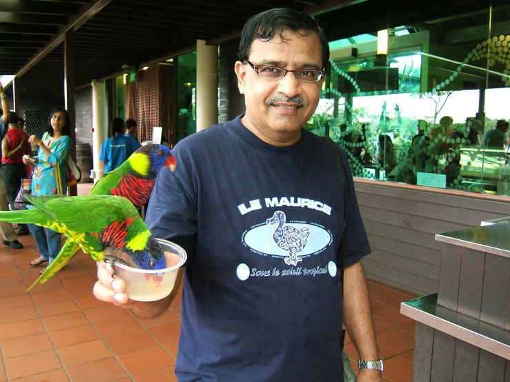 a man holding a bowl filled with food and a parrot on his arm