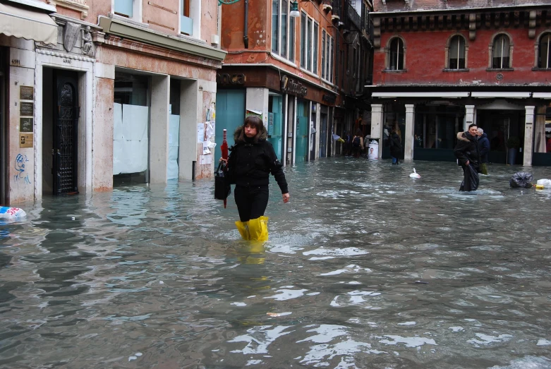 two people walking in flood waters past buildings