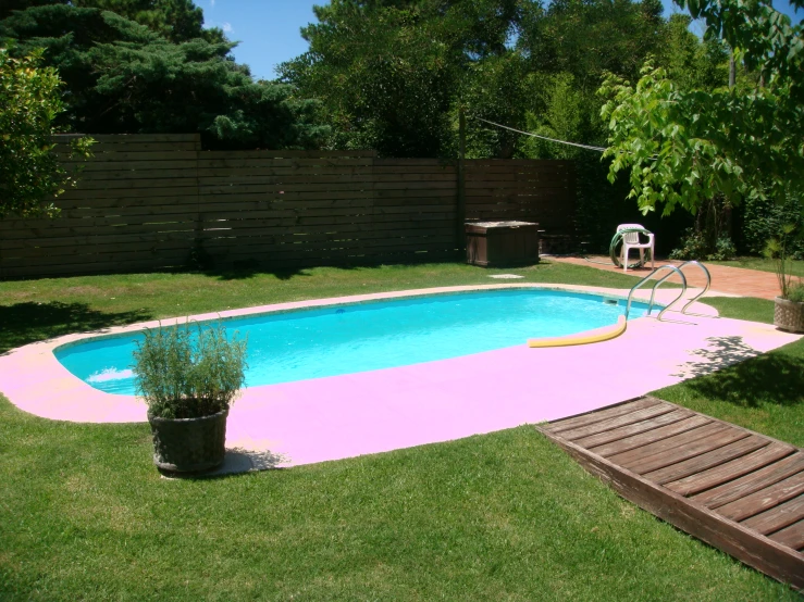 a backyard swimming pool in an area with a fence, lawn and chairs