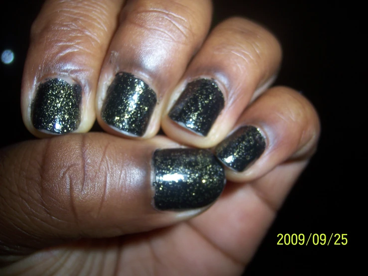a hand holding up a black manicure with gold glitter