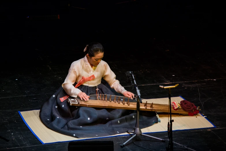 a woman sits on the ground while playing a musical instrument