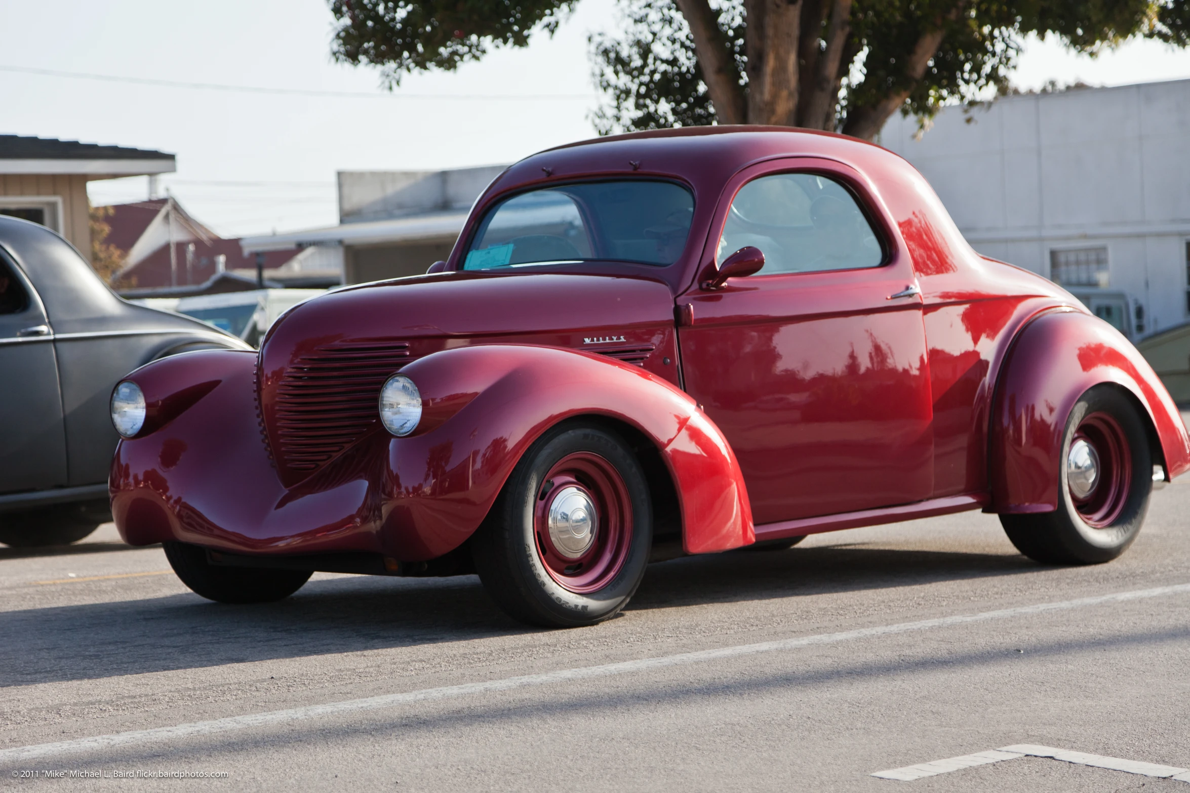 an old classic red car is driving down the street