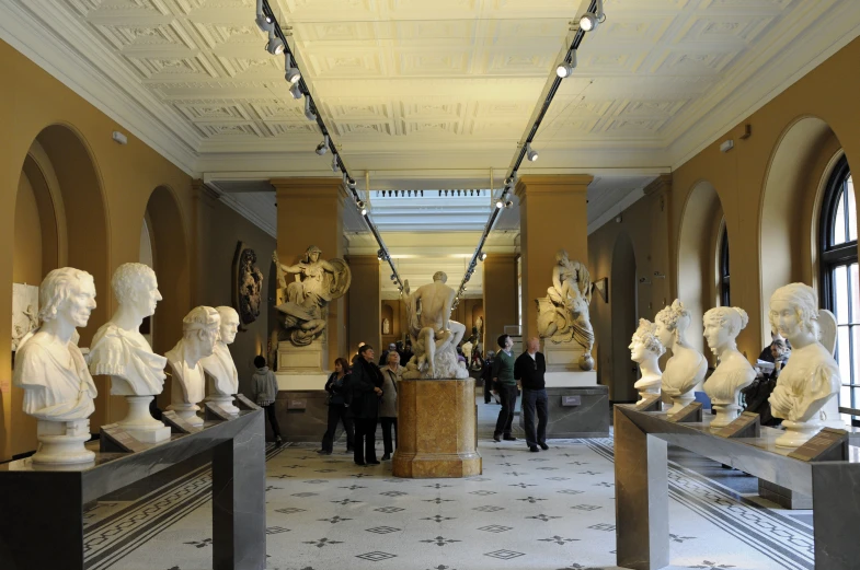 large room with white marble sculptures and people walking around