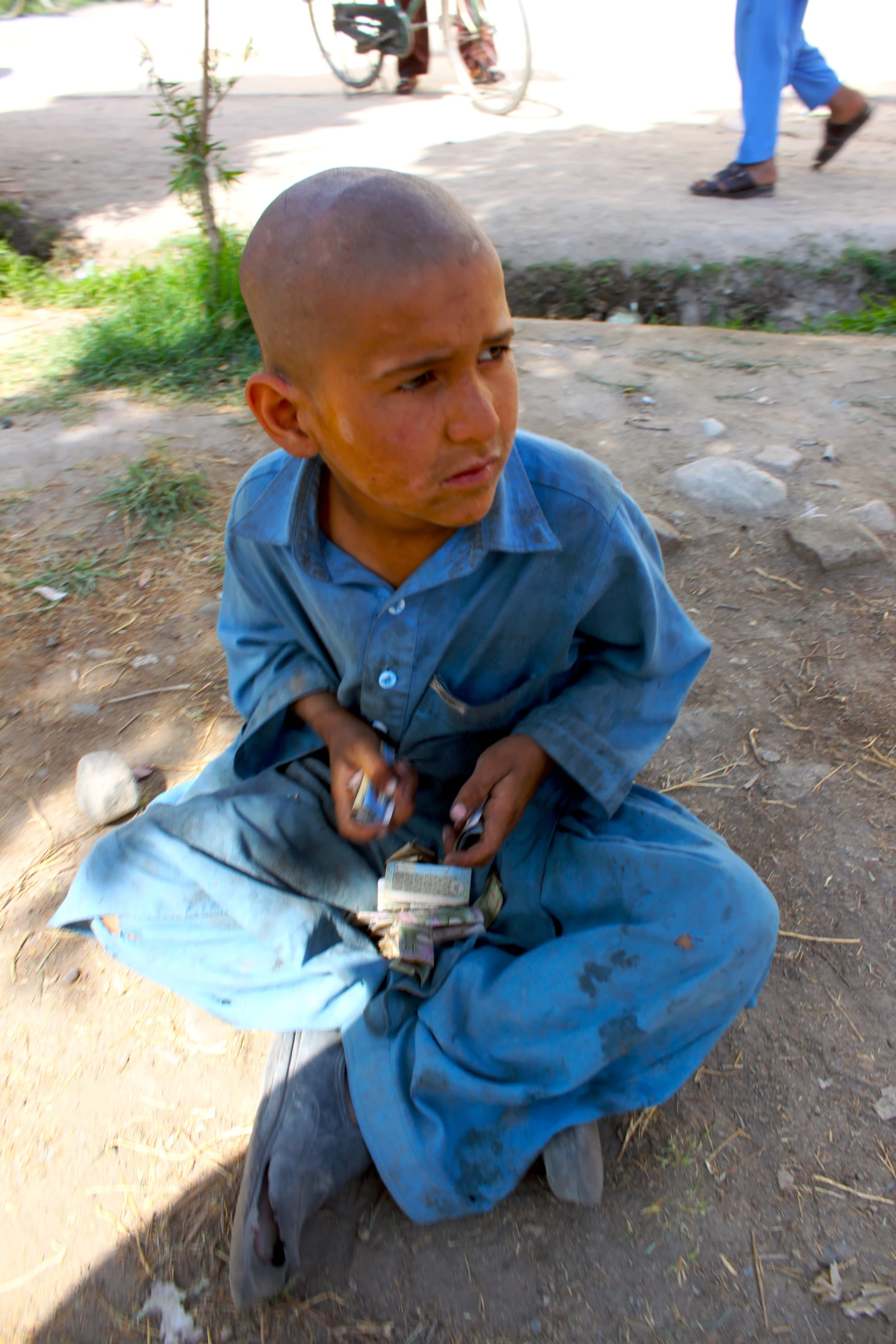 a small boy sitting on the ground holding a cellphone