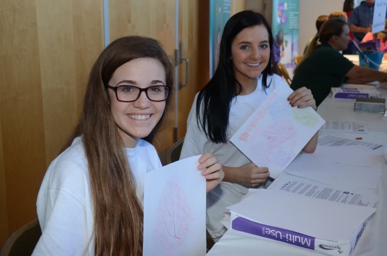 two women hold up pamphlets next to a table full of letters