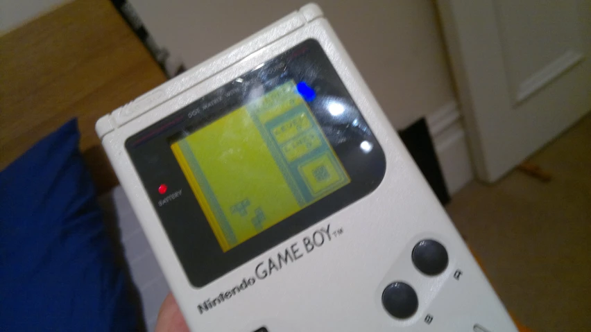 a white gameboy is displayed in front of a blue pillow