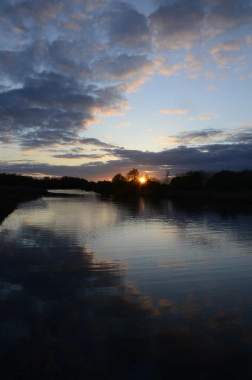 a cloudy sky and the sun setting over a body of water