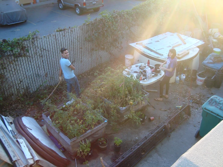 a man and a woman standing in a backyard garden with a car and various lawn supplies