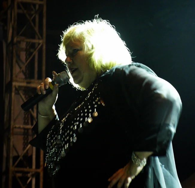 a person in black shirt singing on stage with microphone