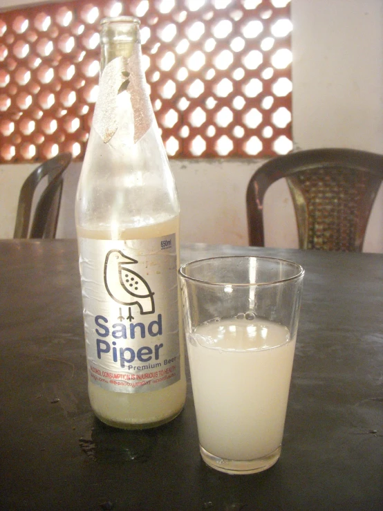 a glass filled with milk sits on a table near a bottle of sand piper