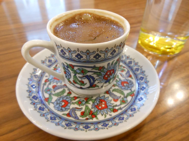 a close up of a cup on a plate with a glass behind it