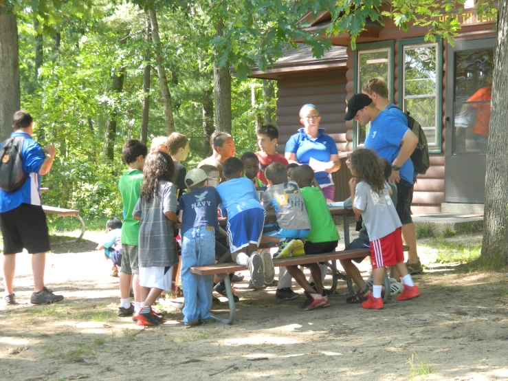 a man talking to a group of young children sitting at a picnic table
