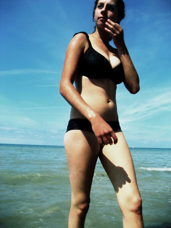 a woman standing in the ocean while wearing a bikini top