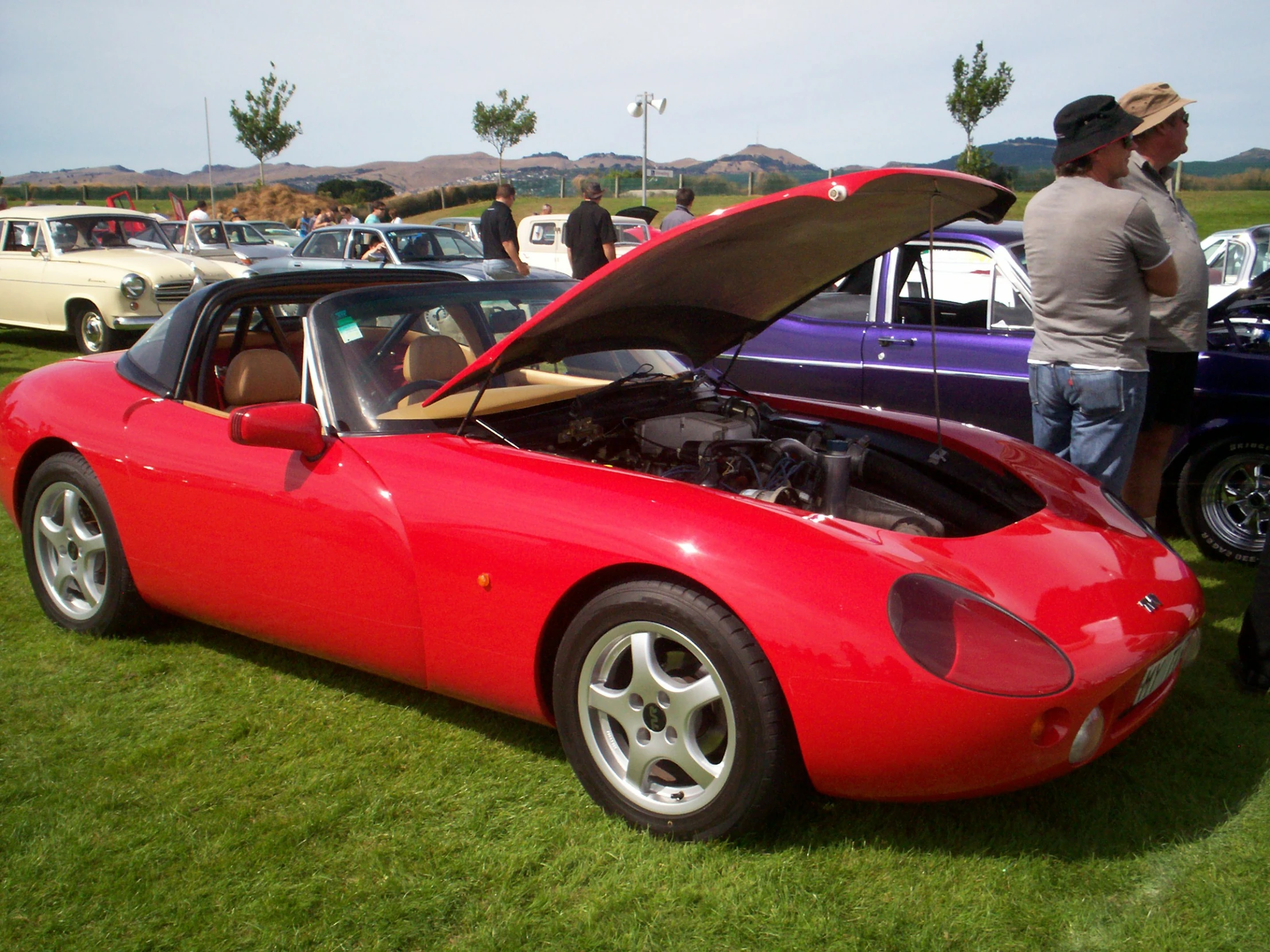 a classic red car with a top open on a green lawn