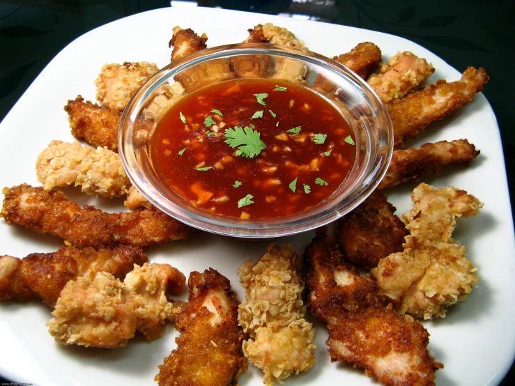 a bowl of chili sauce with chicken wings on a white plate
