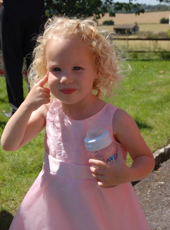 little girl with blonde hair in pink dress holding water bottle