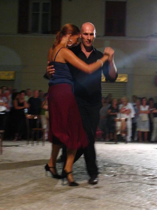 a man and a woman dance together on a cobblestone area, while people watch