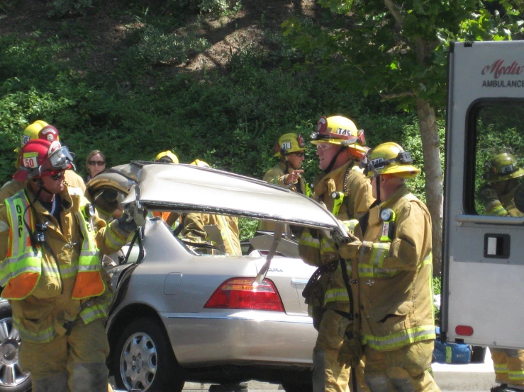 some firemen wearing gear and talking near a car