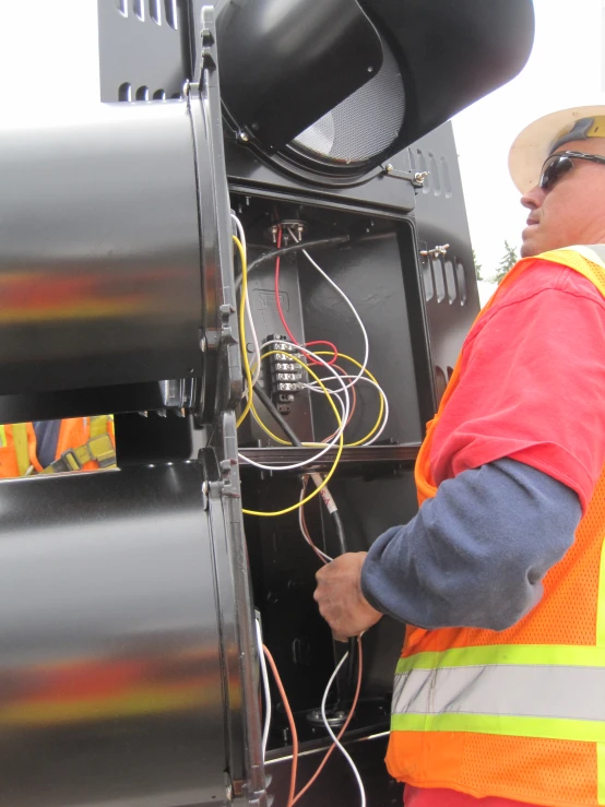 a man in a safety vest inspects some wires attached to a vehicle