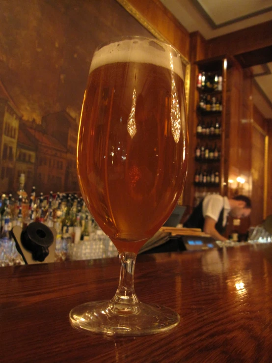 a glass of beer on a bar with a man behind it