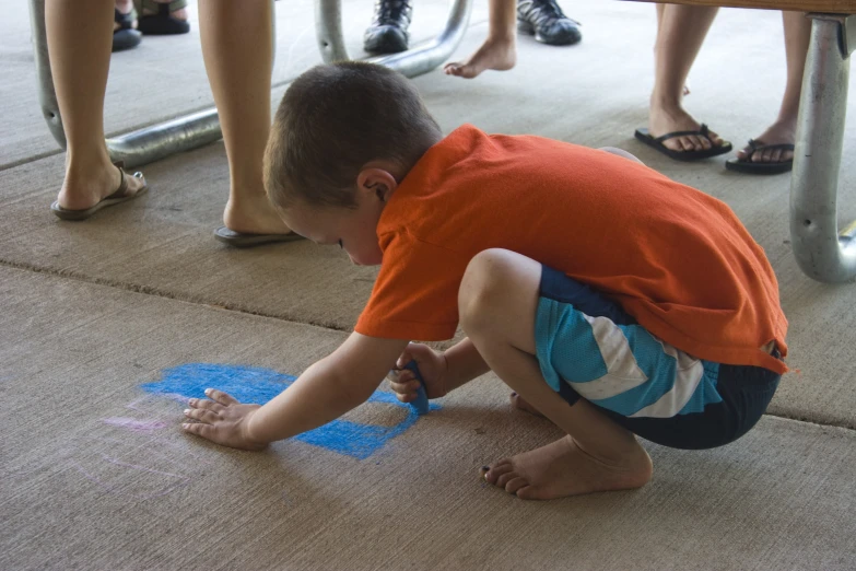 a small boy playing on the floor with blue chalk