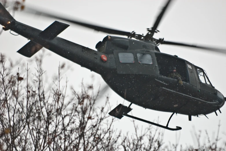 a military helicopter is flying above some trees