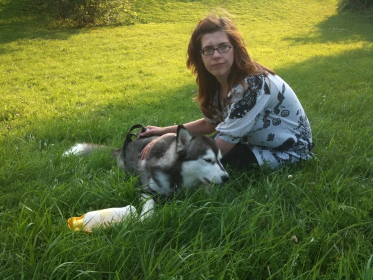 a woman kneeling down on the grass next to her dog