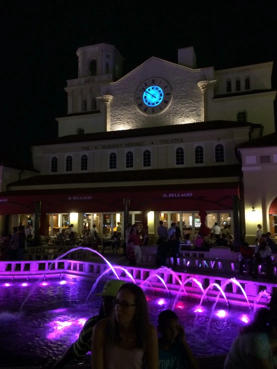 people sitting and standing around at a festival with water spraying from fountains