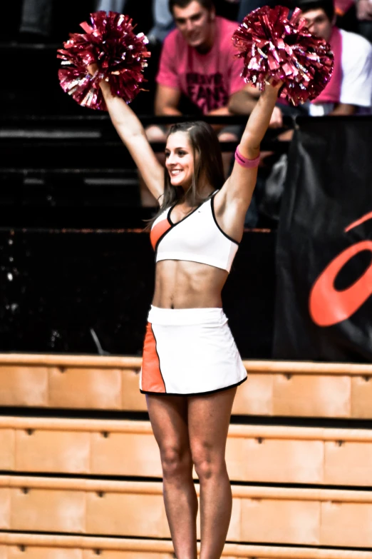 a woman in white and orange is holding up two cheerleaders