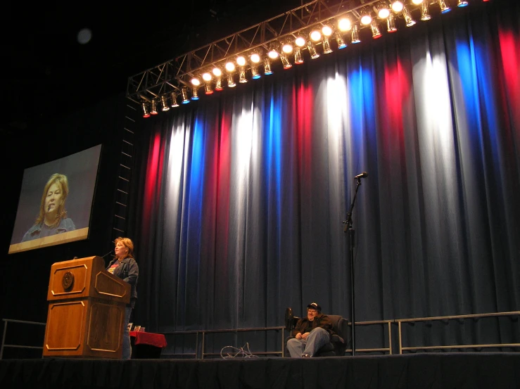 some people are sitting at a table on stage with one person standing up and speaking