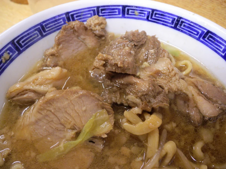 a bowl of meat noodle soup with a blue border