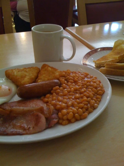 the breakfast plate with bacon, beans, eggs and bread is on the table