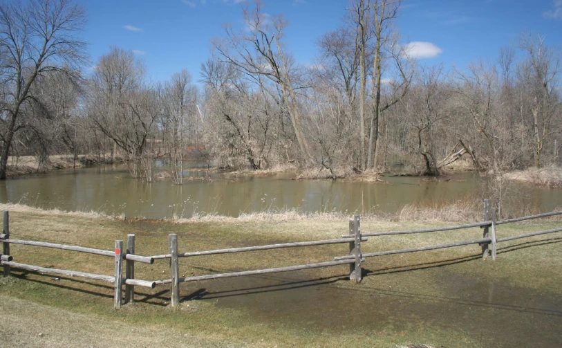 a lake behind a wooden fence surrounded by grass
