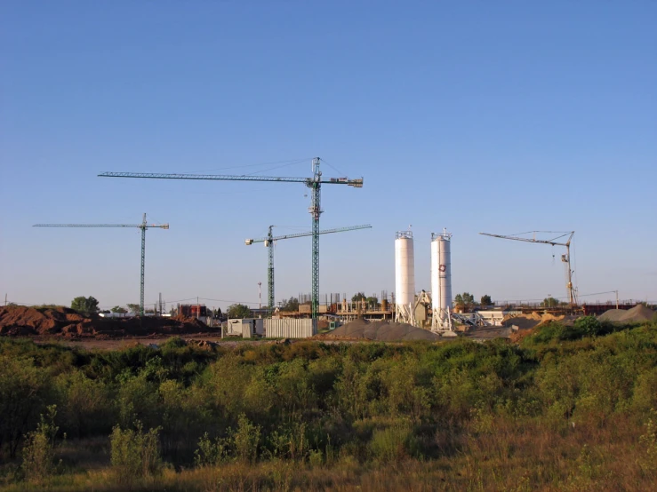 four cranes above a construction site on a clear day