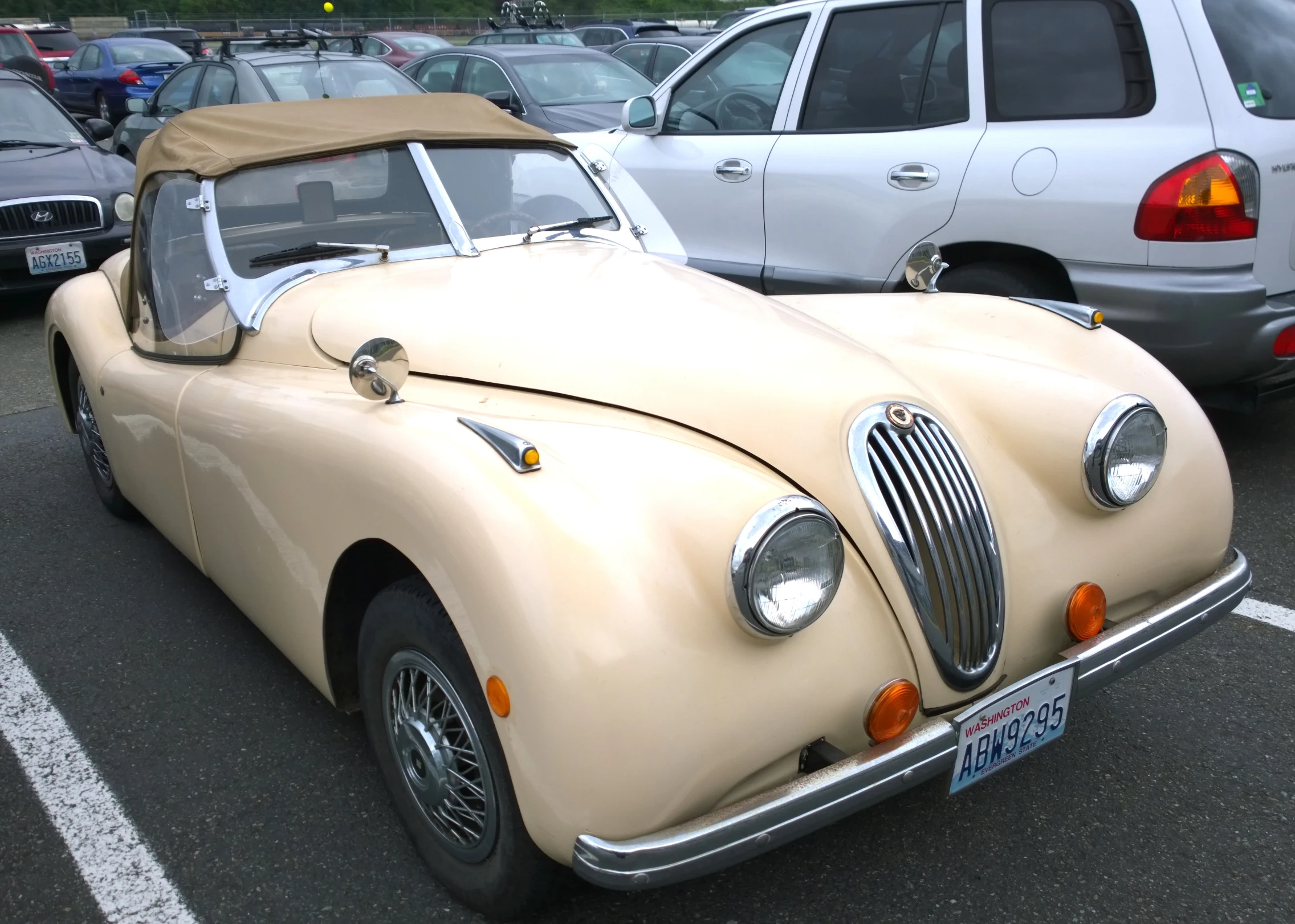 a tan antique sports car is parked in a parking lot