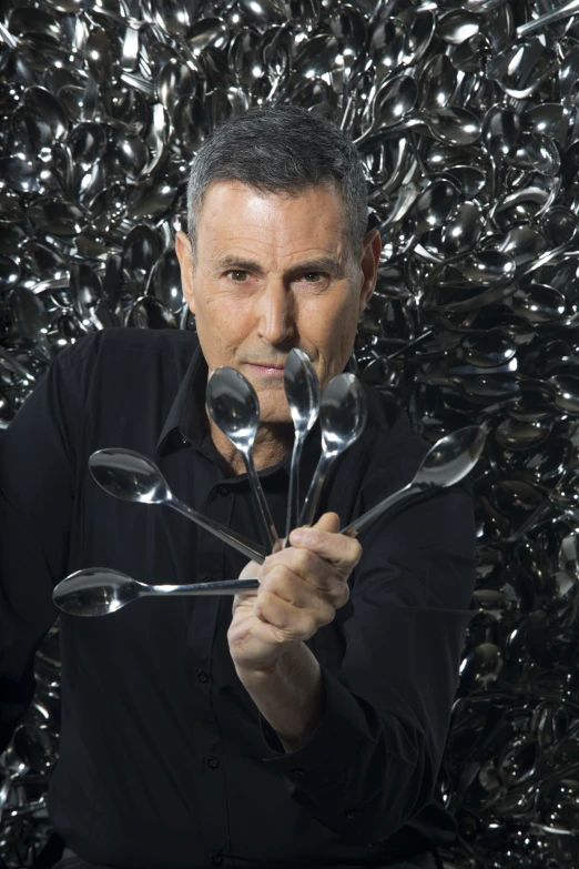 man holding spoons with metal objects in the background