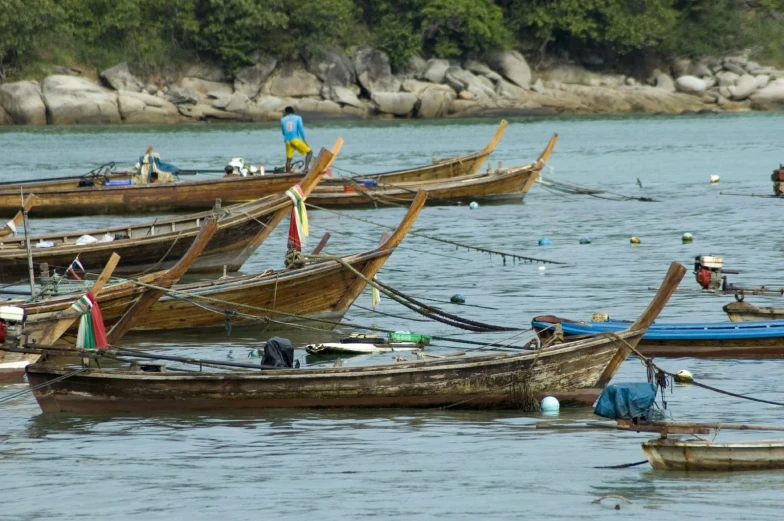 some people standing around a group of small boats in the water