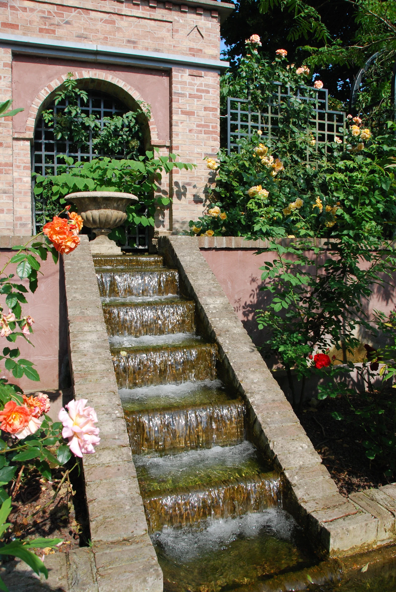 a garden with large water fountain and roses around it